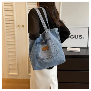 Detailed view of light blue washed denim tote bag with leather logo on front pocket