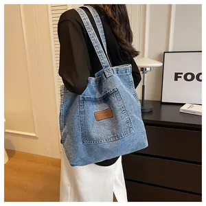 Detail of blue denim tote bag texture featuring a brown leather patch and large front pocket