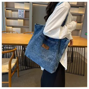 Detail of vintage blue washed denim tote bag with brown leather patch in a library setting