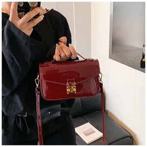 Detail of burgundy glossy patent leather handbag with gold buckle and top handle