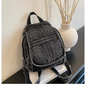 Detailed view of dark grey washed denim backpack with decorative stitching on white pedestal