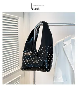 Détail d'un sac hobo noir avec rivets argentés suspendu sur un fond blanc épuré