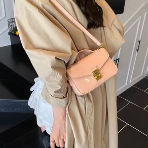 Pink patent leather crossbody handbag with gold buckle shown on a model in a trench coat