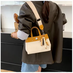 Detalle del bolso tote de lona bicolor con ribete de cuero y borla de cuentas de madera