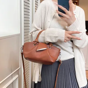 Caramel brown leather bucket bag with pleated texture and silver leaf buckle shown on model