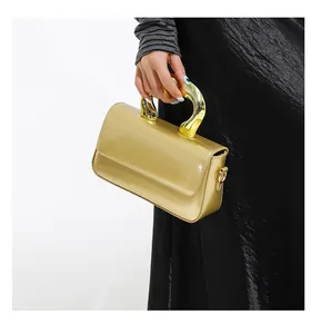 Detail of glossy gold handbag with artistic geometric metal handle and silk dress