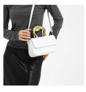 Detail of artistic gold curved metal handle on a white leather shoulder bag