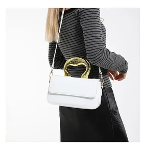 Detail of white glossy shoulder bag with artistic gold wave handle on a female model