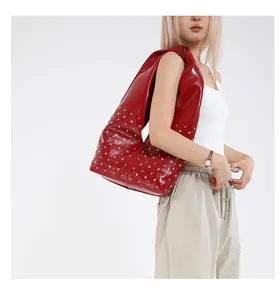Détail d'un sac Hobo en cuir verni rouge avec rivets argentés porté par un modèle