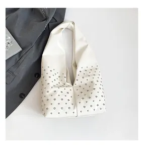 Détail du sac hobo blanc avec rivets argentés sur fond de tissu luxueux et texturé