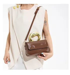 Detail of dark brown patent leather handbag with artistic golden metal handle and fine strap