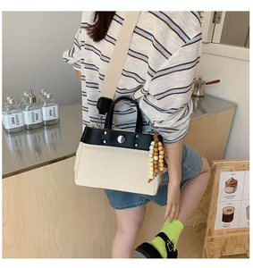 Detalle de bolso tote de lona con ribete de cuero negro y detalles de remaches de plata