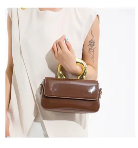 Close-up of a dark brown patent leather handbag featuring a bold gold C-shaped handle