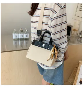 Detalle del bolso tote de lona con ribete de cuero negro, remaches y colgante de madera