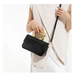 Detail of black patent leather handbag featuring a bold gold round metal top handle