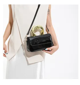 Detail of glossy black patent leather handbag with artistic gold sculptural handle