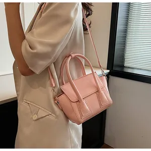Detail of a pink leather handbag with distinctive cylindrical handles worn by a model