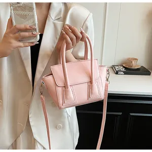 Detailed view of pink leather handbag with square stitched handle and adjustable strap