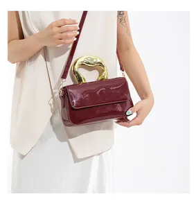 Close-up of wine red patent leather handbag with a sculptural gold metal handle