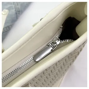 Nahaufnahme der cremefarbenen Webhandtasche mit silbernem Reißverschluss und PU-Leder-Textur