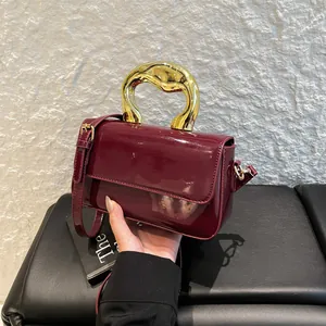 Chic burgundy patent leather shoulder bag with sculptural gold handle and sleek flap closure
