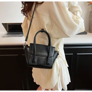 Model wearing a black matte leather handbag with adjustable strap and top handles