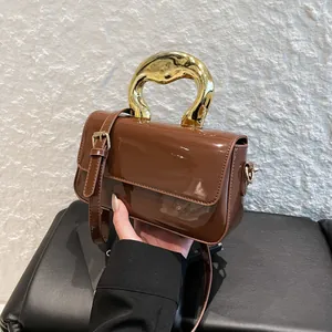 Chic brown patent leather crossbody bag with oversized gold metal handles and flap closure