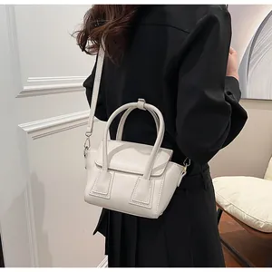 Detail view of cream white leather crossbody bag with trapezoid flap design on model