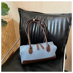 Détail du sac Boston en denim bleu avec anses en cuir marron sur une chaise en cuir