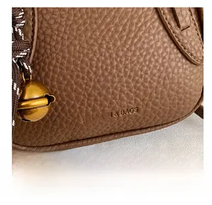 Detail der braunen Leder-Handtasche mit goldener Glocke und gewebtem Griffdekor