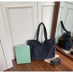 Detail of grey washed denim tote bag with star relief and laptop for size reference