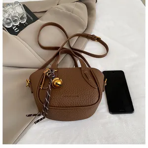 Detailansicht der braunen Lederhandtasche mit Litschi-Muster und goldenen Anhängern