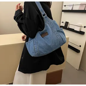 Detail of blue denim tote bag featuring brown leather patch and side pocket on the model
