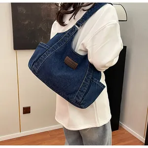 Detailed close-up of dark blue denim hobo bag featuring brown leather fashion label