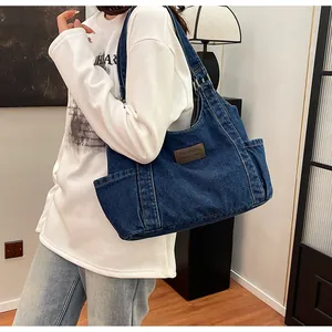Detail of blue denim tote bag showing side pocket, leather label and adjustable strap