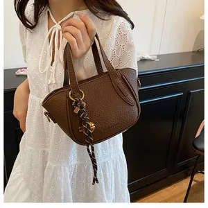 Detail einer dunkelbraunen Lederhandtasche mit Goldbeschlägen und gewebtem Quastenanhänger