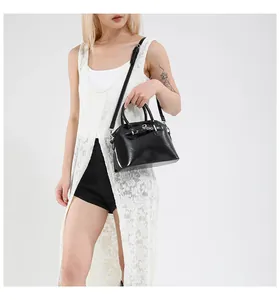 Chic black glossy shell bag worn by model with adjustable shoulder strap and silver hardware