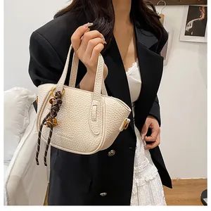 Detail der cremeweißen Beuteltasche mit Kieselstruktur und dekorativem Glockenanhänger