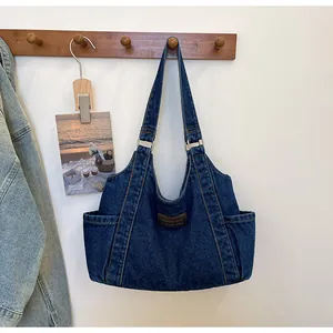 Detail view of large denim tote bag featuring side pockets and a brown leather logo patch