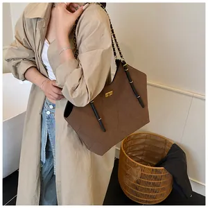 Detail of dark brown suede tote bag with diamond quilting and gold chain strap on model