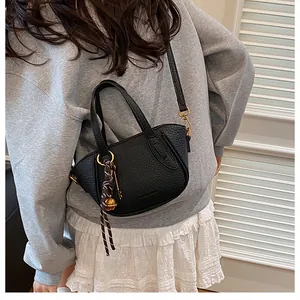 Detailansicht einer schwarzen Handtasche aus Leder mit dekorativem Anhänger an einem Model