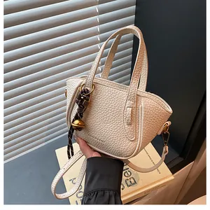 Detailansicht der cremefarbenen Leder-Eimertasche mit Lychee-Muster und Goldglocke