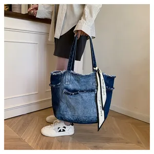 Détail du sac cabas en denim effiloché avec anse ornée d'un foulard en soie élégant