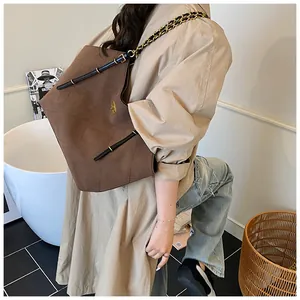 Detail of a brown quilted suede tote bag with golden metal logo and chain strap
