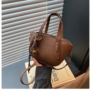 Detail der dunkelbraunen Eimertasche mit Litschi-Muster, Fashion-Logo und Goldteilen