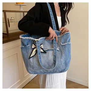 Détail du grand sac cabas en jean bleu avec bords effilochés et nœud décoratif