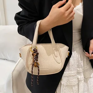 Minimalistische beige Beuteltasche mit Flechtanhänger und kleinen goldenen Glocken