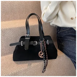 Detail of black suede tote bag featuring silver buckle and woven rope pendant