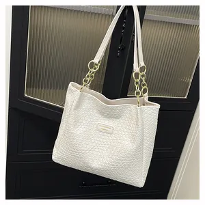 Close-up of white woven texture tote bag with gold chain strap and metal logo
