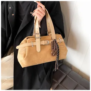 Detail view of mustard yellow suede handbag with metal buckle and decorative charms